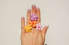 a woman's hand with pink, yellow and orange flowers on it holding up her fingers