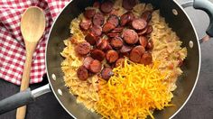 sausage, pasta and cheese in a skillet with a wooden spoon on the side