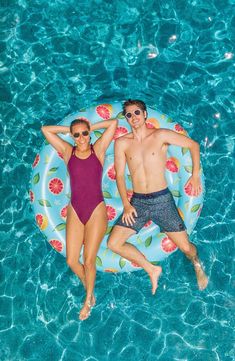 a man and woman laying on an inflatable flowered pool float, smiling at the camera