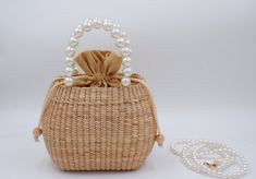 a wicker purse with pearls on the handle and chain around it, next to a white beaded necklace