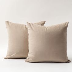 two beige pillows sitting next to each other on a white surface with no one in the photo