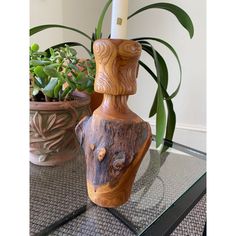 a wooden candle holder sitting on top of a glass table next to potted plants