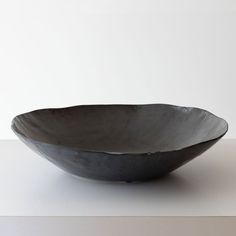 a large black bowl sitting on top of a table next to a white wall and floor