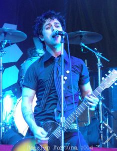 a man singing into a microphone while holding a guitar in front of him on stage