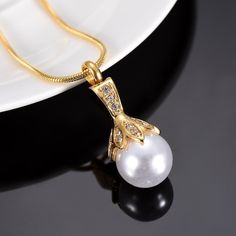 a white pearl and diamond pendant on a gold chain with a black plate in the background