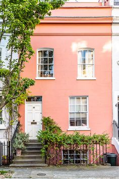 a pink house with white doors and windows next to a tree in front of it