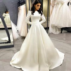 a woman standing in front of a mirror wearing a white wedding dress with long sleeves