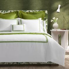 a bed with green and white comforters in a bedroom next to a lamp on a table