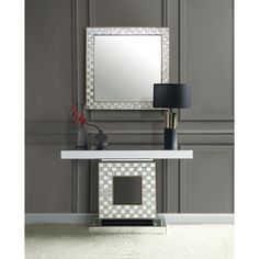 a white table with a mirror and lamp on it in front of a gray wall