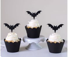 three cupcakes with white frosting and black bats on top are sitting on a cake plate