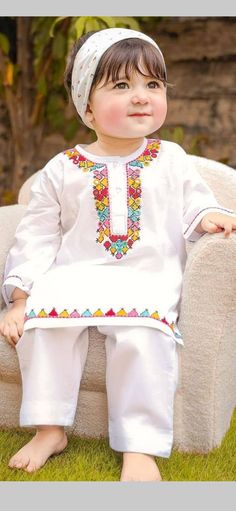 a little boy sitting on top of a couch wearing a white outfit with colorful beads