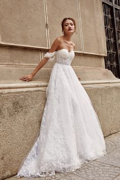 a woman in a white wedding dress leaning against a wall with her hand on the side