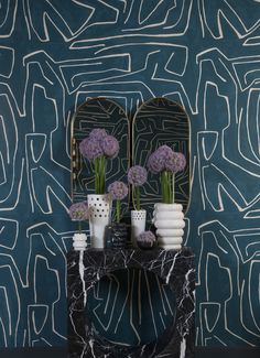 two vases with flowers sit on a marble table in front of a blue wall