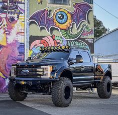 a large black truck parked in front of a building with graffiti on the wall behind it