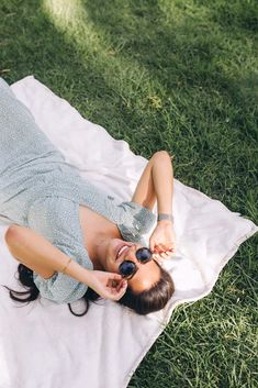 a woman laying on top of a white blanket in the grass with her eyes closed