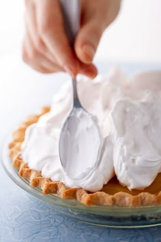 a person holding a spoon over a pie with whipped cream on it's crust