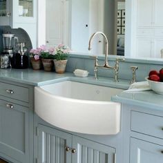 a white sink sitting under a kitchen window next to a counter top with bowls of fruit on it