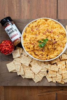 a bowl of dip surrounded by crackers, tomatoes and other snacks on a cutting board