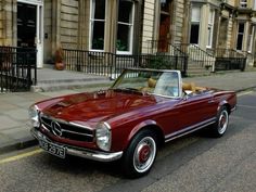 an old red convertible car is parked on the street