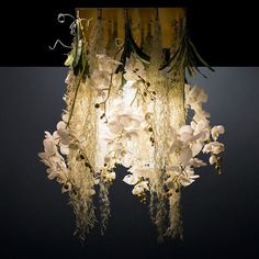 a chandelier with white flowers hanging from it's sides in a dark room