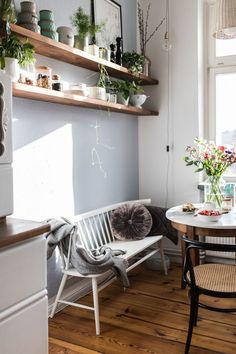 a table and chairs in a room with shelves on the wall behind them, plants are sitting on top of the tables