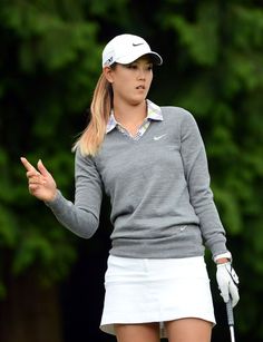 a woman in grey shirt and white skirt holding a golf club with her hand up