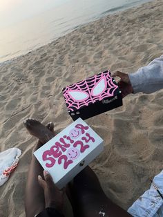 two people are sitting on the beach with a box that says hello kitty in pink