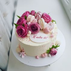 a white cake with pink roses and macaroons on top