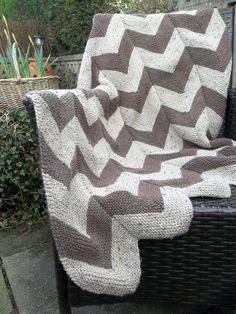 a chair with a blanket on top of it in front of some plants and bushes