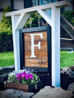 a wooden sign with the letter f hanging from it's side in front of some flowers