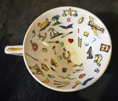 a white bowl with colorful designs on it sitting on a black counter top next to a yellow and red object