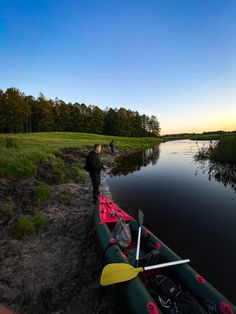 a man standing next to a kayak on the side of a river at sunset