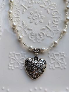 This handmade piece brings a fun elegant twist on the vintage Y2K heart pendant. The heart hangs between hand a beaded strong of white and clear beads and faux vintage pearls. A trendy Y2K necklace to bring a little style and romance to your life. White Beaded Necklaces For Valentine's Day, Valentine's Day White Beaded Necklaces, Vintage Dangle Jewelry With Heart Beads, Handmade Pearl Heart Pendant Jewelry, White Round Beads Jewelry With Heart Charm, White Jewelry With Heart Charm And Round Beads, Heart-shaped Pearl Beaded Chain Jewelry, Handmade White Beaded Necklaces For Valentine's Day, Handmade Heart-shaped Pearl Jewelry