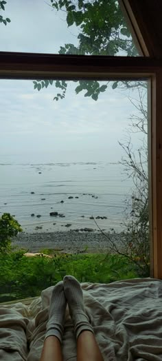 a person laying in bed with their feet up looking out the window at the ocean