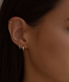 a close up view of a woman's ear with two small gold hoop earrings