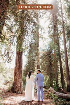 a bride and groom standing in the middle of a forest holding hands while looking at each other