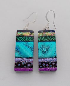 the earrings are made from glass and have purple, blue, and green designs on them