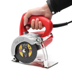 a hand holding a circular saw on top of a red object with a black handle