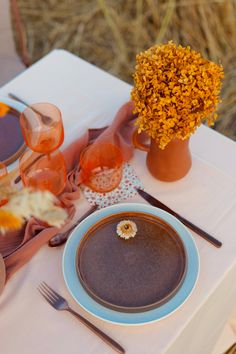 the table is set with plates, silverware, and orange flowers in vases