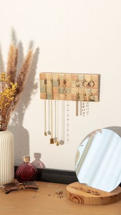 a mirror, vase with flowers and jewelry on a table next to a white wall