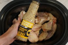 a hand holding a bottle of chicken marinade in a slow cooker