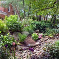 a garden with rocks and flowers in the foreground, along side a brick house