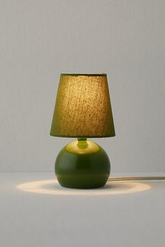 a green lamp sitting on top of a table next to a white wall and floor