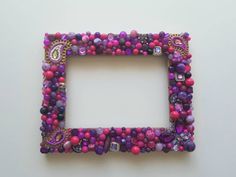 a purple and pink beaded photo frame sitting on top of a white table next to a wall