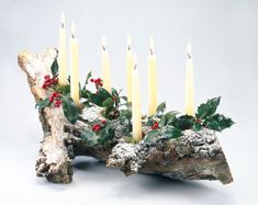 a group of candles sitting on top of a piece of wood with holly and berries