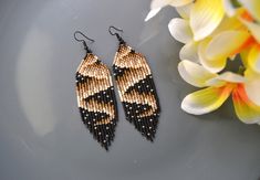 a pair of beaded earrings sitting on top of a gray plate next to flowers