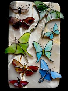 several different colored glass butterflies sitting on top of a white tile surface with black background