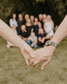 two people holding hands in front of a group of people sitting on the grass outside