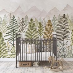 a baby crib in front of a wall mural with trees and mountains on it