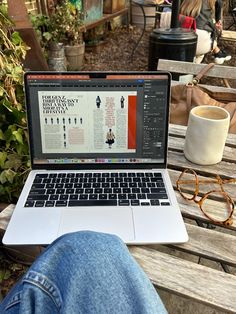 an open laptop computer sitting on top of a wooden bench next to a cup of coffee